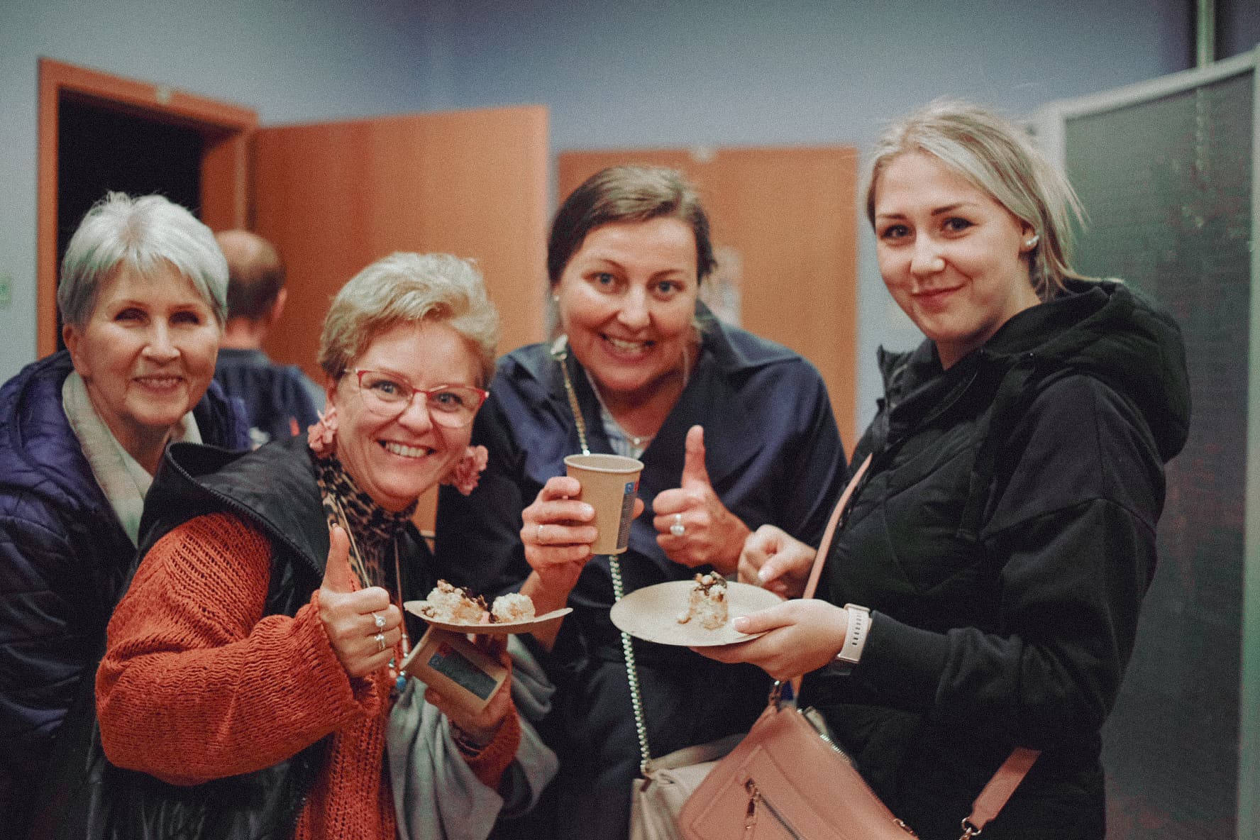 4 kobiet uśmiechających się do kamery, gdzie 3 z nich trzymają w ręku talerz i kubek